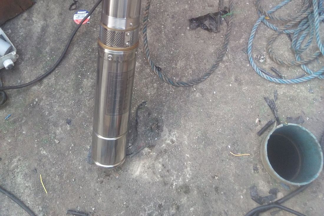 Bomba sumergible de acero inoxidable en el suelo, junto a la boca de un tubo de pozo