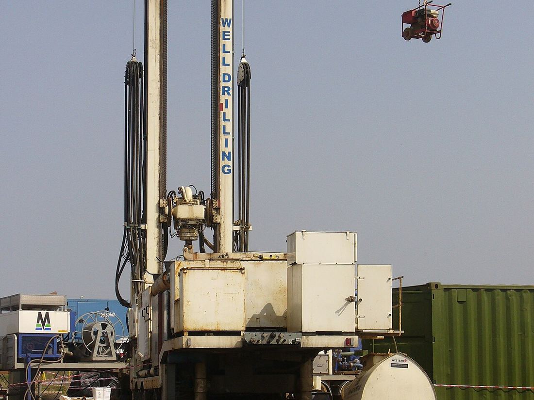 Torre de una máquina perforadora de pozos de agua en faena, con mangueras y contenedores alrededor